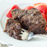 one of the low carb brownies on a plate with small bite broken off on fork. Plate also includes a side of cut strawberries