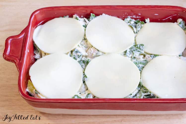 slices of provolone cheese on top spinach and artichoke chicken casserole before baking in red casserole dish
