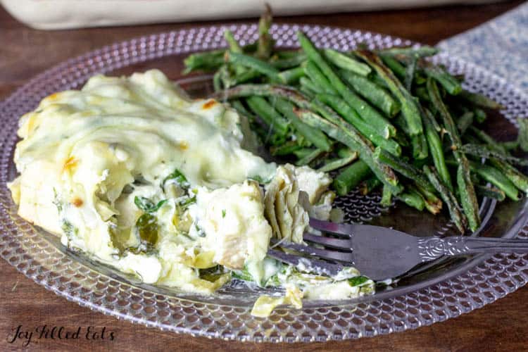 plate of spinach and artichoke chicken casserole with fork. served with a side of green beans