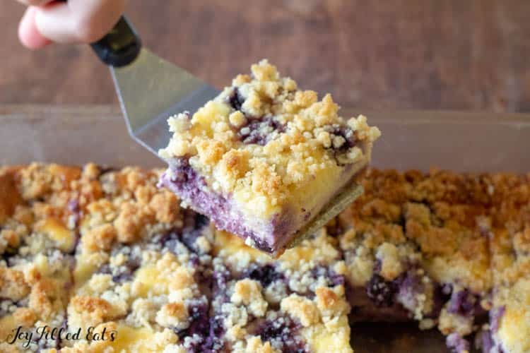 Hand with serving spatula taken middle square piece of lemon blueberry cheesecake Crumb bar out of baking dish