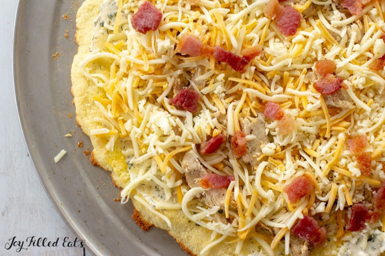 Close up of coconut flour pizza crust with toppings of cheese, bacon and chicken