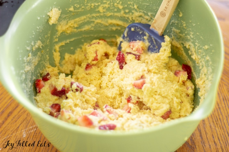 Mixing bowl of batter with berry pieces and spatula.