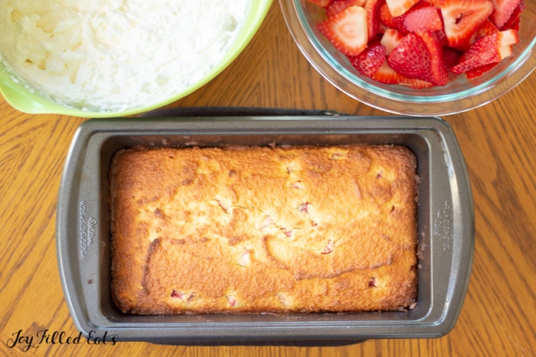 Pound Cake in a loaf pan with a bowl of whipped cream and strawberries