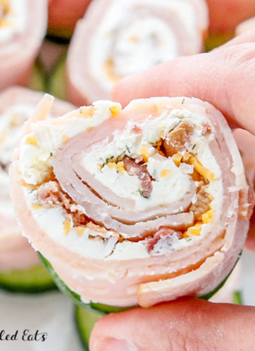 Close up of hand holding Turkey Bacon Ranch Pinwheels on a cucumber