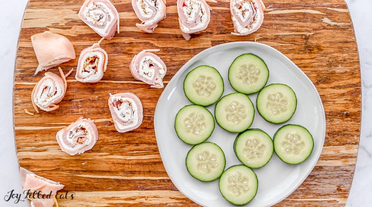 pinwheels on a cutting board with sliced cucumber on a plate next to them
