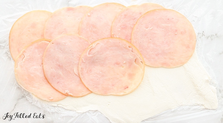 cream cheese spread on plastic wrap with deli meat