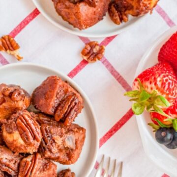 Overhead shot of two plates of keto gorilla bread on red and white plaid napkin with a bowl of strawberries