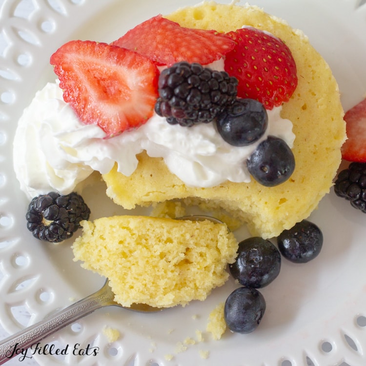 keto vanilla mug cake topped with whipped cream and mixed berries with a bite of cake resting on a fork