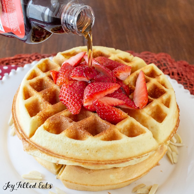 Syrup being poured over 2 strawberry topped low carb waffles.
