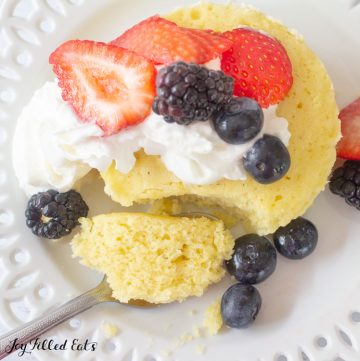 vanilla mug cake topped with whipped cream and mixed berries with a bite of mug cake resting on a fork