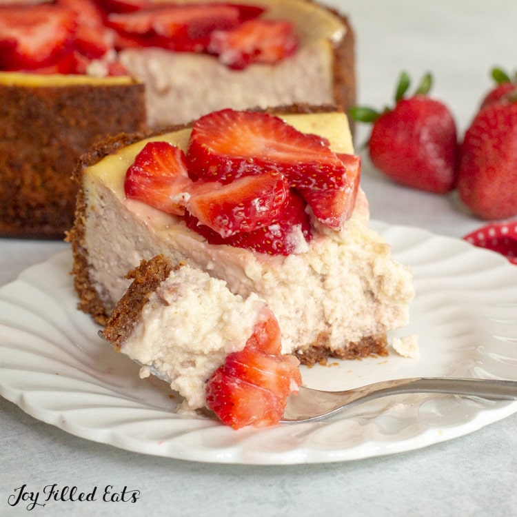 a slice of Keto Strawberry Cheesecake on a small plate with a bite on a fork