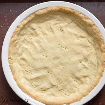 close up on overhead view of low carb pie crust baked into white pie plate with fork holes punched in