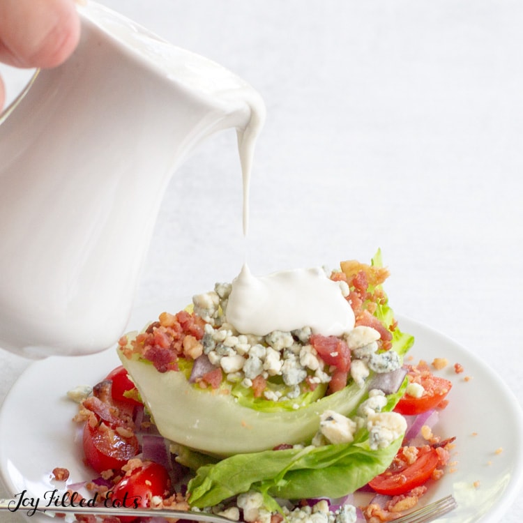 hand pouring dressing from a small pitcher onto a salad