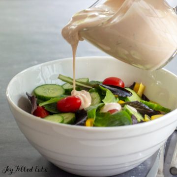 pitcher pouring keto thousand island dressing on top of a green salad in a white bowl