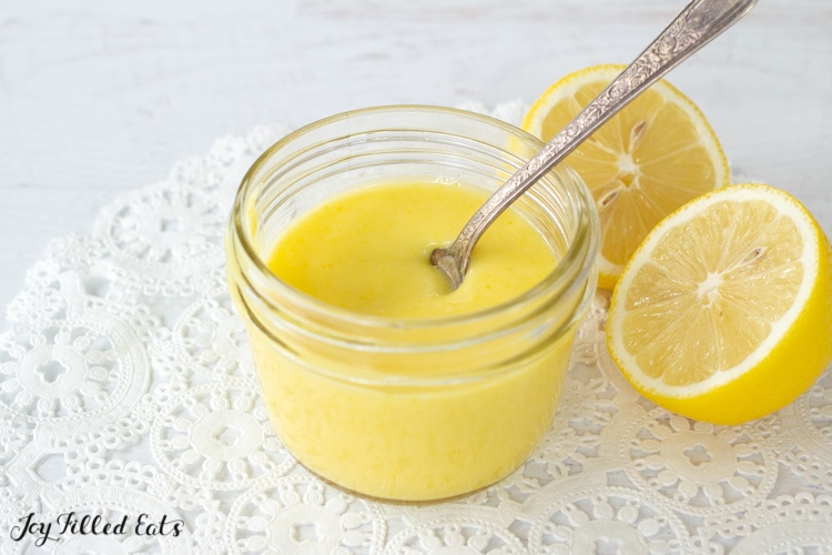 jar of keto lemon curd with a spoon next to halved lemon