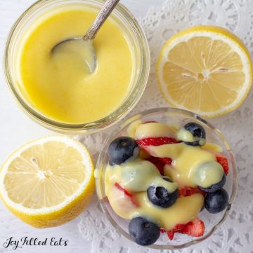 jar of keto lemon curd with a spoon next to halved lemon and bowl of berries