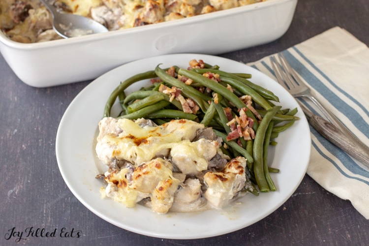 close up of a plate with baked chicken marsala casserole and green beans