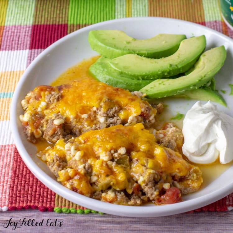 Mexican taco casserole serving on a plate with sour cream and avocado slices