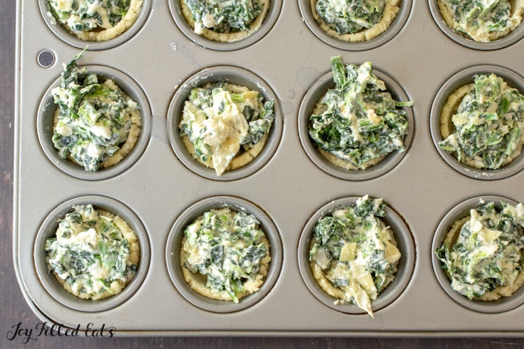 a mini muffin tin with dough cups filled with keto spinach artichoke dip