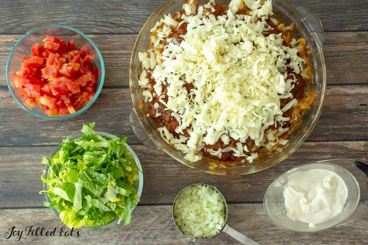 the baked keto taco pie with salsa and shredded cheese on top andsmall bowls of toppings around it