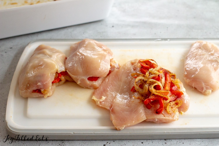 raw chicken cut to make a flap with cooked peppers and onions