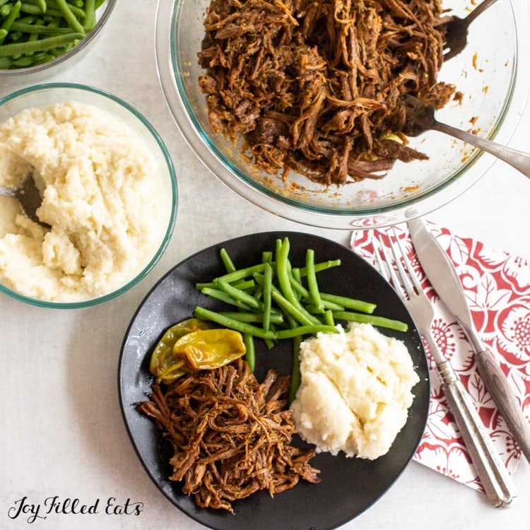 overhead shot of serving bowls of keto mississippi pot roast, mashed cauliflower, and green beans