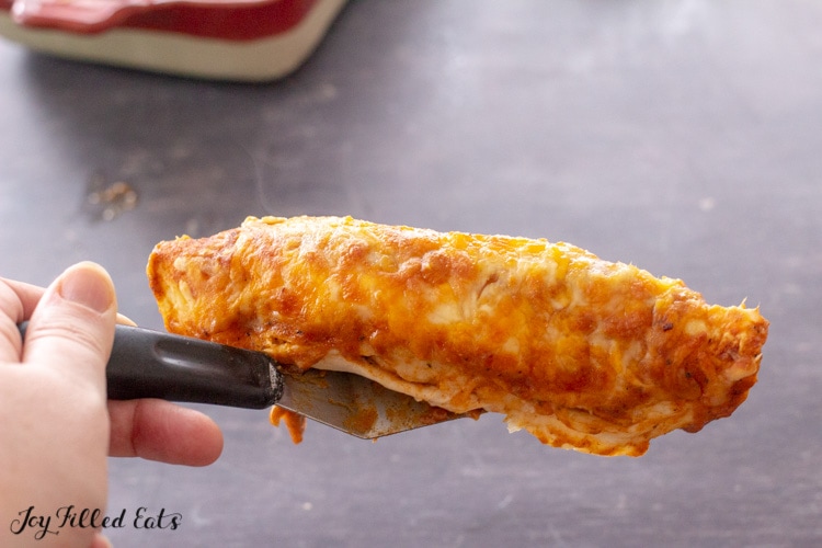 a hand lifting up a spatula with an enchilada