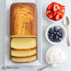 keto pound cake on a serving platter with small bowls of whipped cream and berries