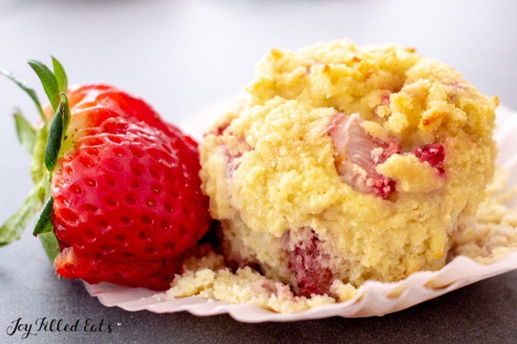 one of the keto strawberry muffins on the paper liner next to a fresh berry