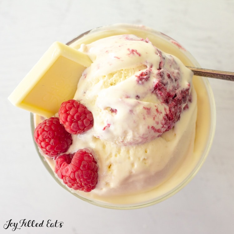 close up of bowl of white chocolate raspberry ice cream topped with a white chocolate square and fresh raspberries