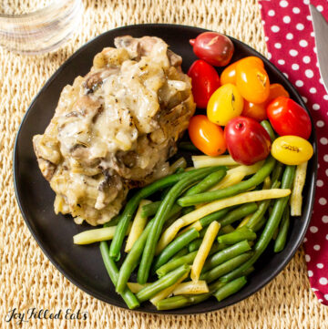 overhead shot of one of the keto smothered pork chops on a plate with green beans and tomatoes
