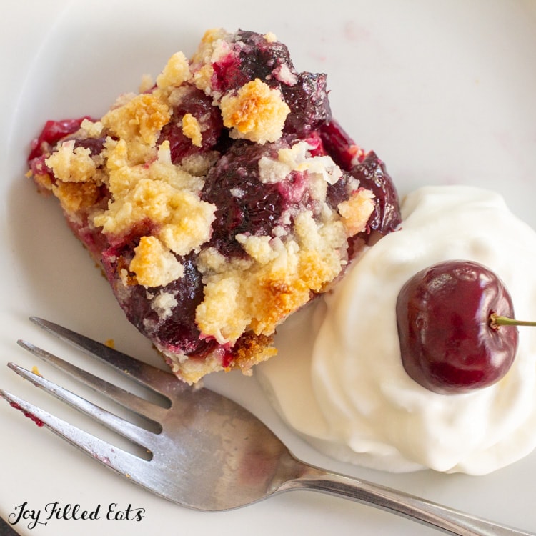 one of the keto cherry pie bars on a plate with whipped cream, a cherry, and a fork