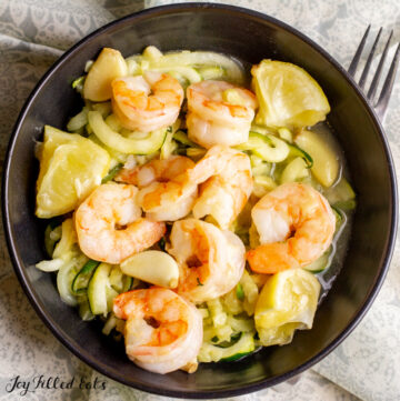 overhead view of black shallow bowl filled with keto shrimp scampi and lemon wedges topped on zucchini noodles