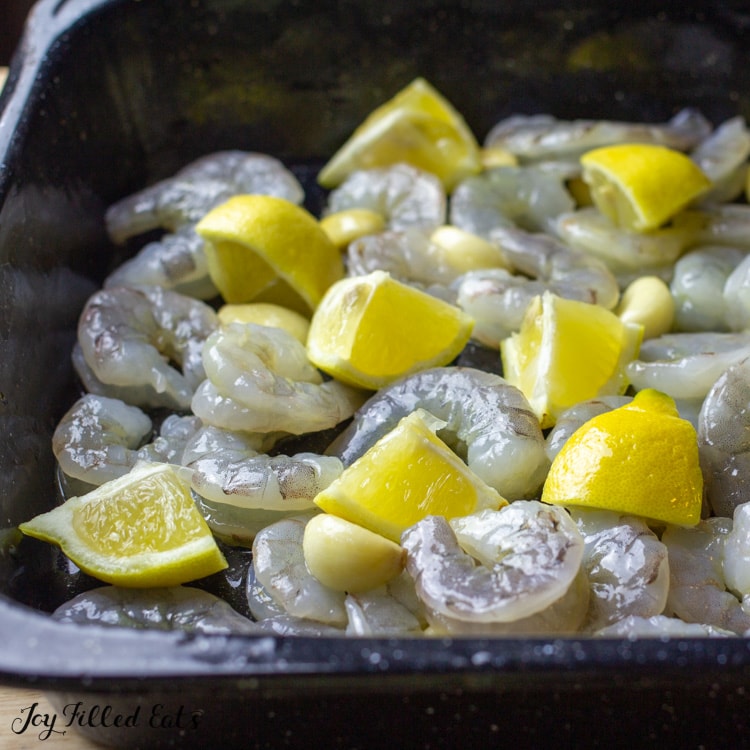 raw shrimp and lemon wedges placed into a baking dish