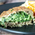 close up of stuffed turkey burger with spinach and three cheeses cut in half on a black plate