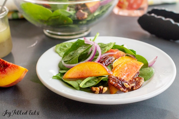 spinach salad with peaches onions and pecans in a bowl