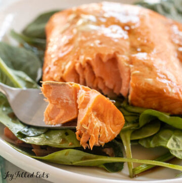 a bite of air fryer frozen salmon on a fork and on top of spinach on a plate