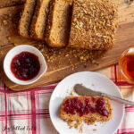 loaf of Gluten Free Sprouted Bread sliced on a cutting board with one piece on a plate with jam