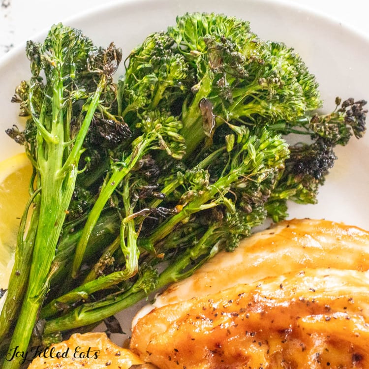 close up of grilled broccolini on a plate with lemon wedge