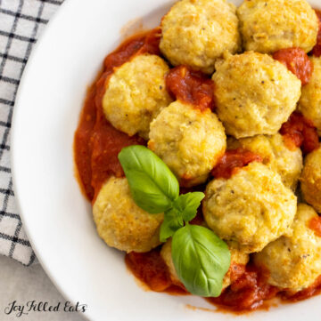 close up of air fryer chicken meatballs on a plate with marinara sauce and basil