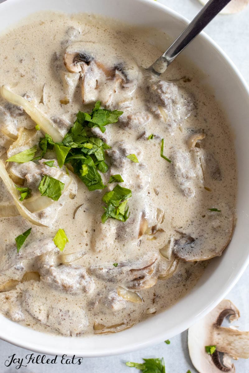 close of the lamb stroganoff in a serving bowl with a spoon and topped with parsley