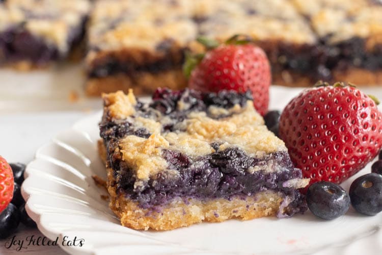 one of the keto blueberry pie bars on a plate with fresh berries