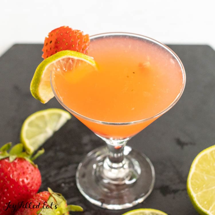 strawberry gimlet in small martini glass with ingredients around it