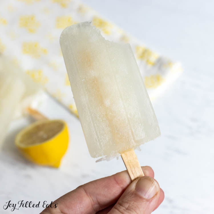 hand holding up a lemon ice pop with a bite missing
