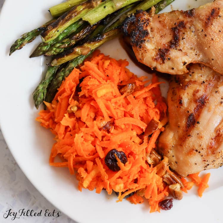 serving of raw carrot salad on a plate with chicken and asparagus