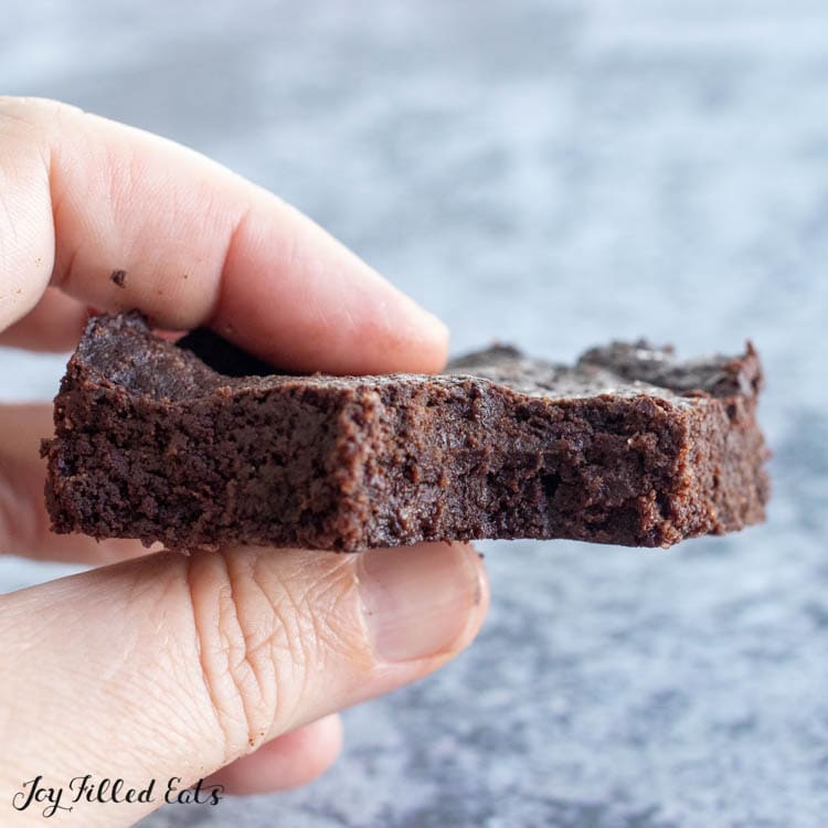 hand holding one of the keto coconut flour brownies close up with a bite missing