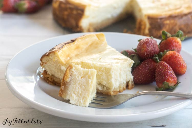 bite of keto cheesecake on a fork next to slice and some strawberries