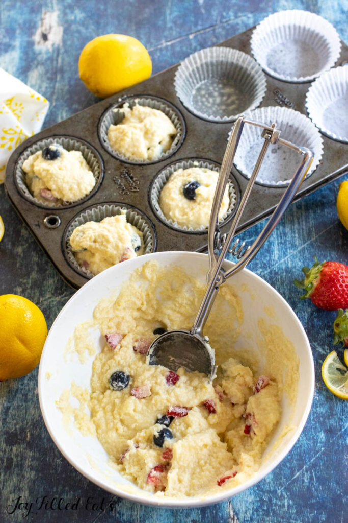 scoop in bowl of batter with muffin tin partially filled behind
