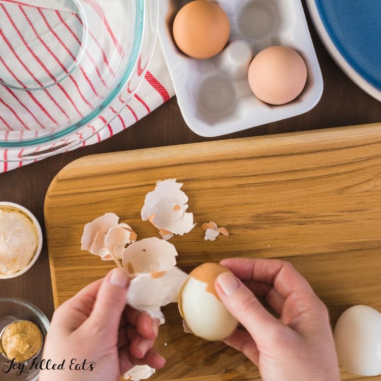 hands peeling hard boiled eggs