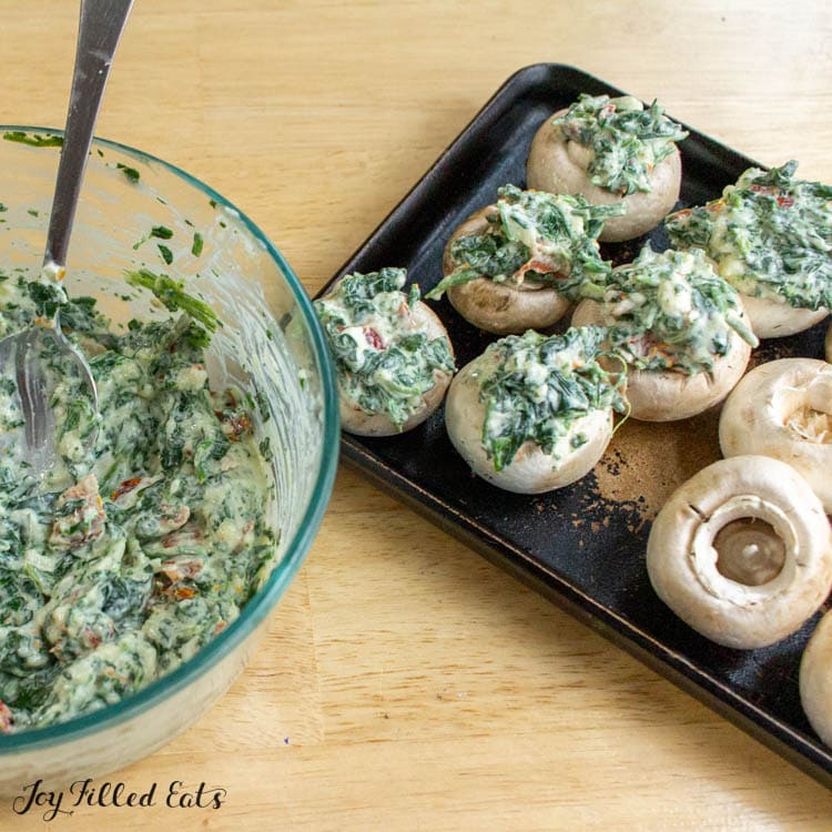 white mushrooms being stuffed with spinach cheese filling